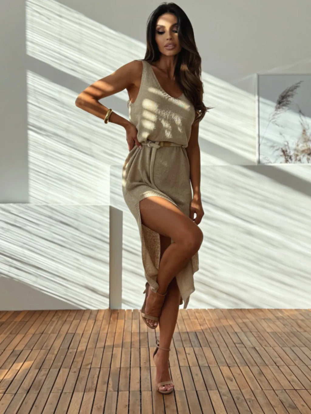 Woman in a beige dress standing on a wooden deck with a white wall background