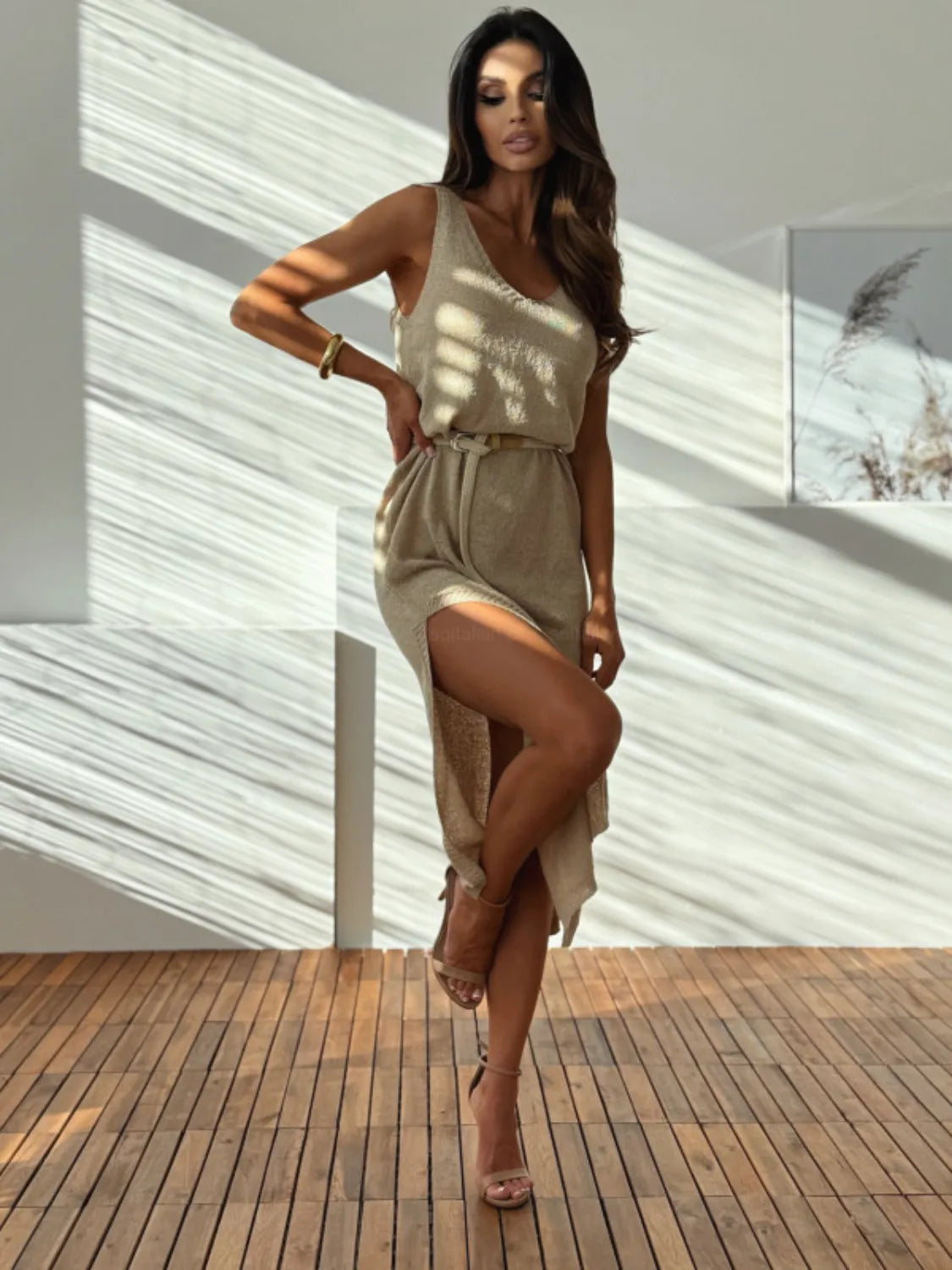 Woman in a beige dress standing on a wooden deck with a white wall background