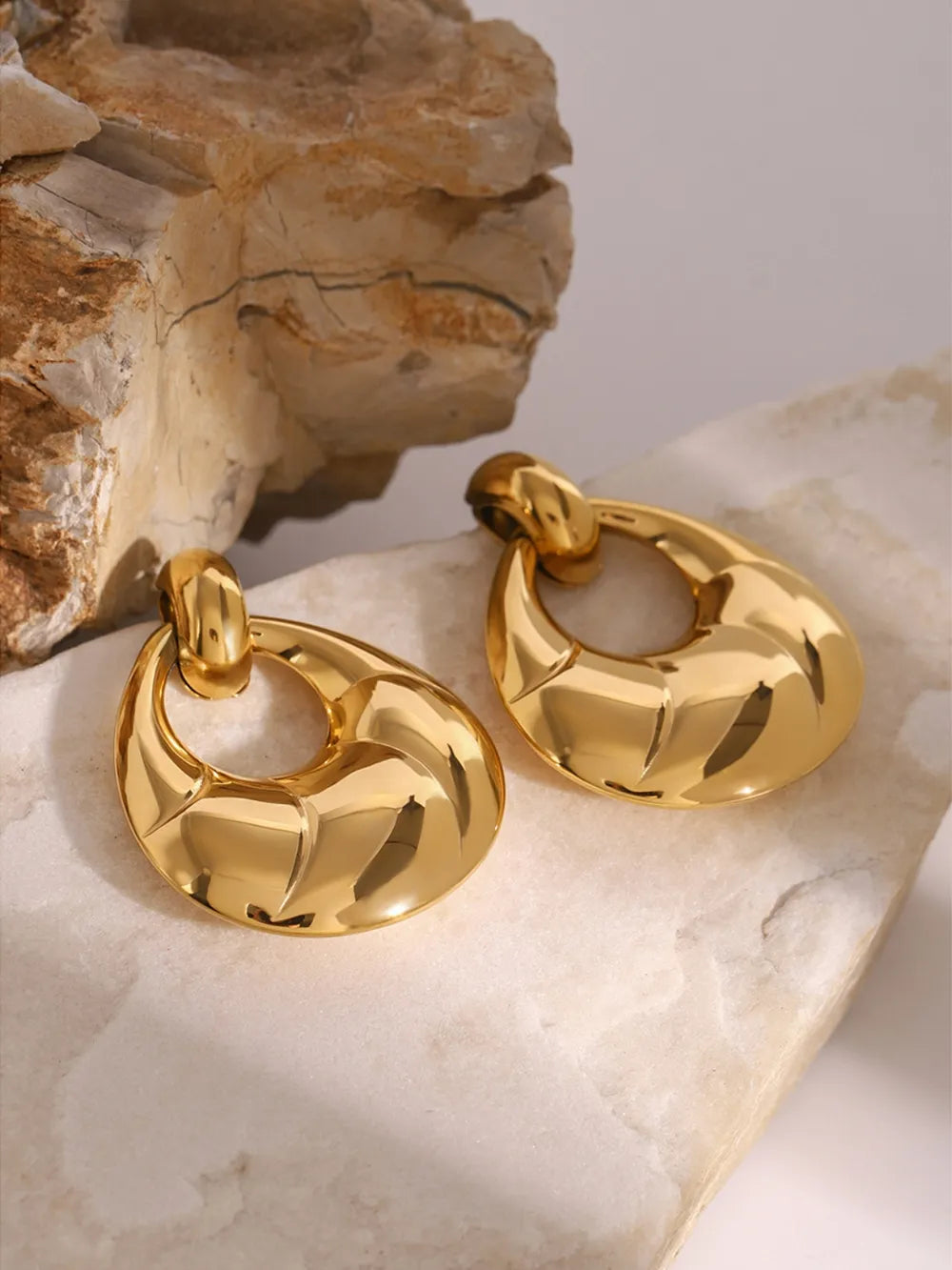 Gold hoop earrings on a textured stone surface