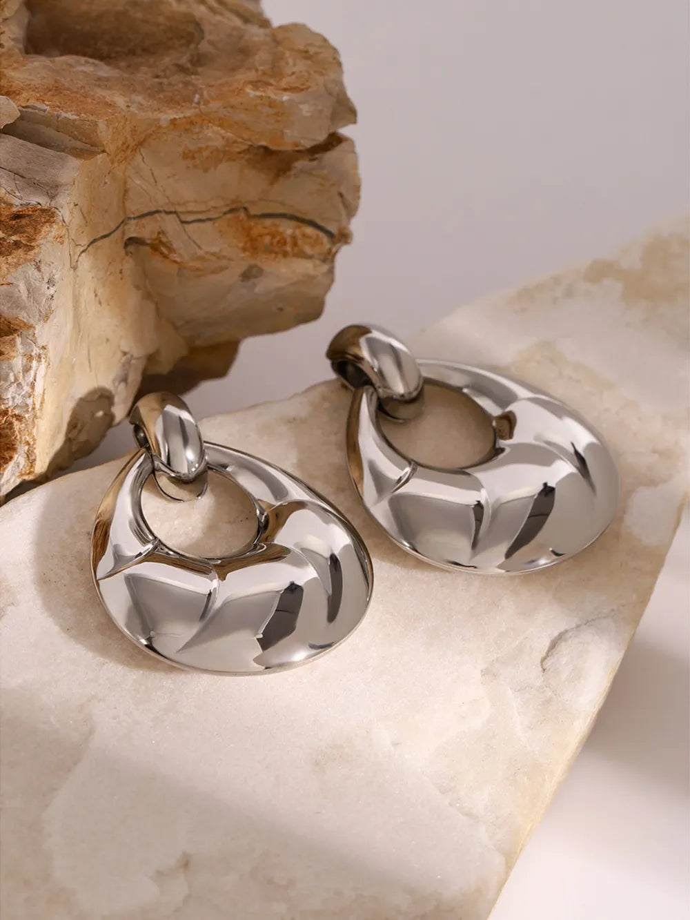 Silver hoop earrings on a textured stone surface