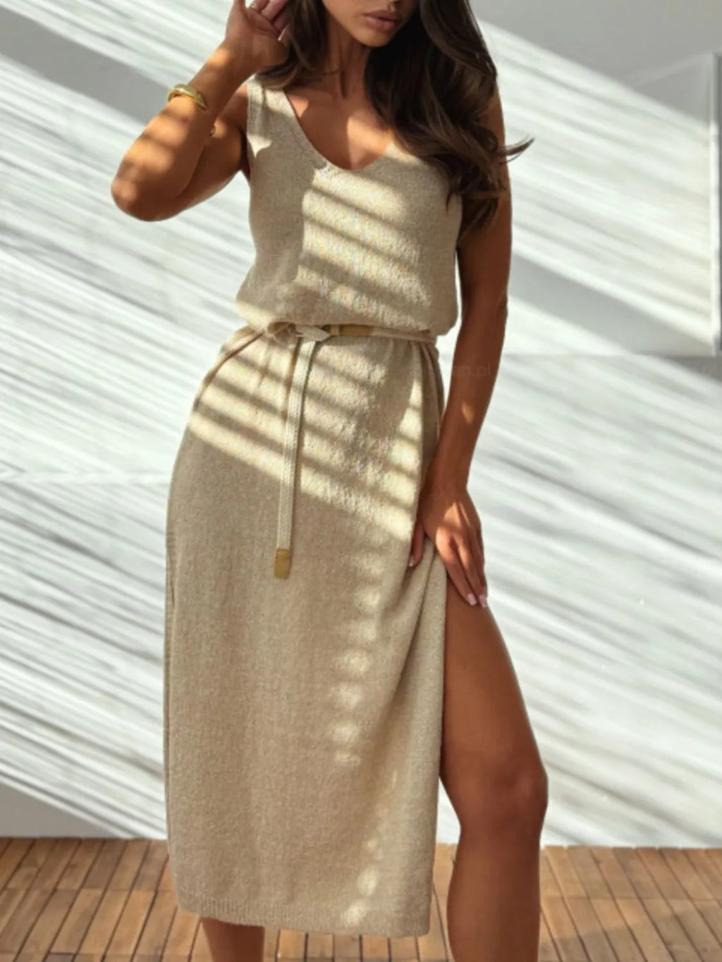 Woman wearing a beige dress with a slit, standing against a white wall.