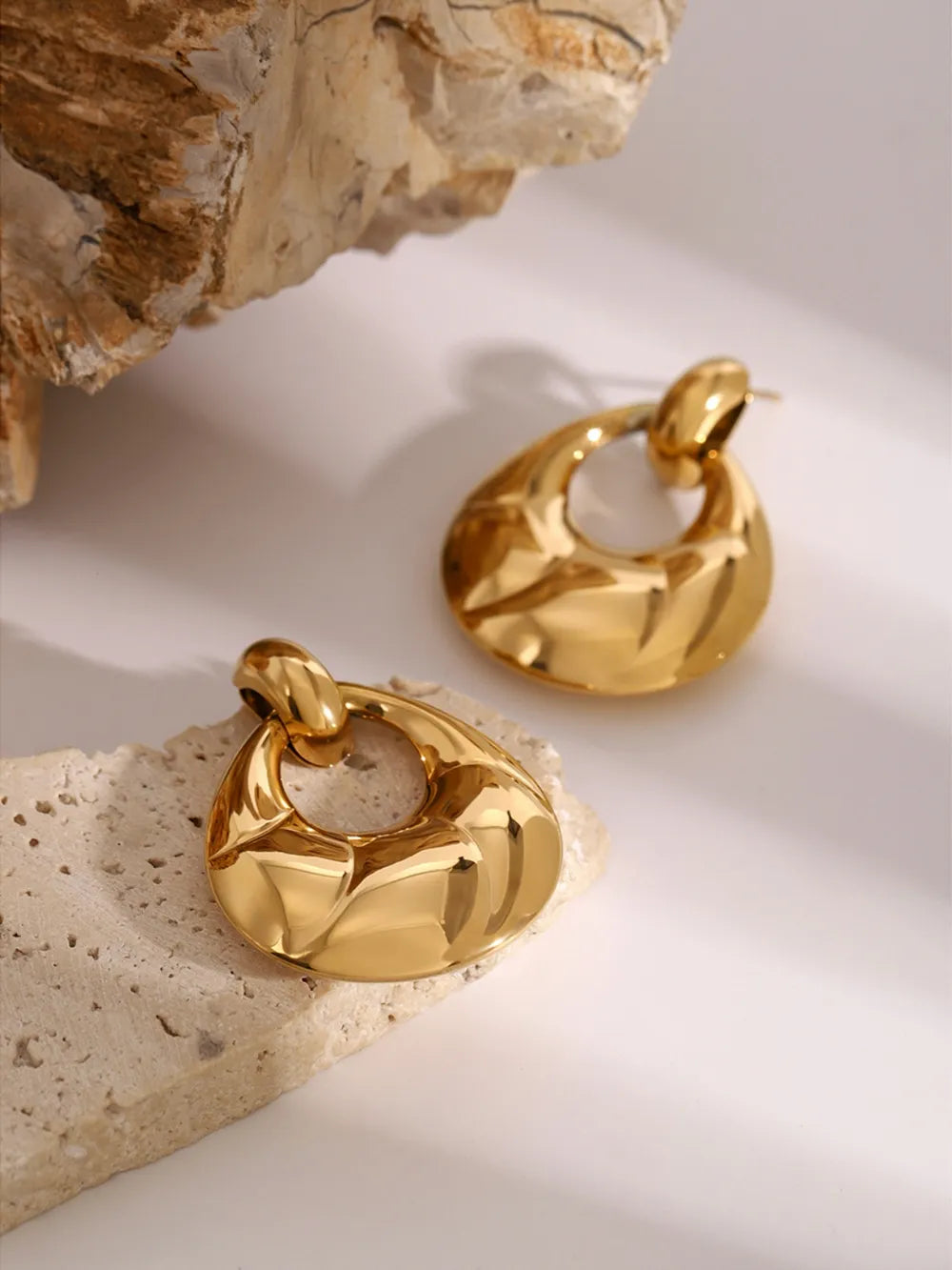 Gold hoop earrings on a textured stone surface