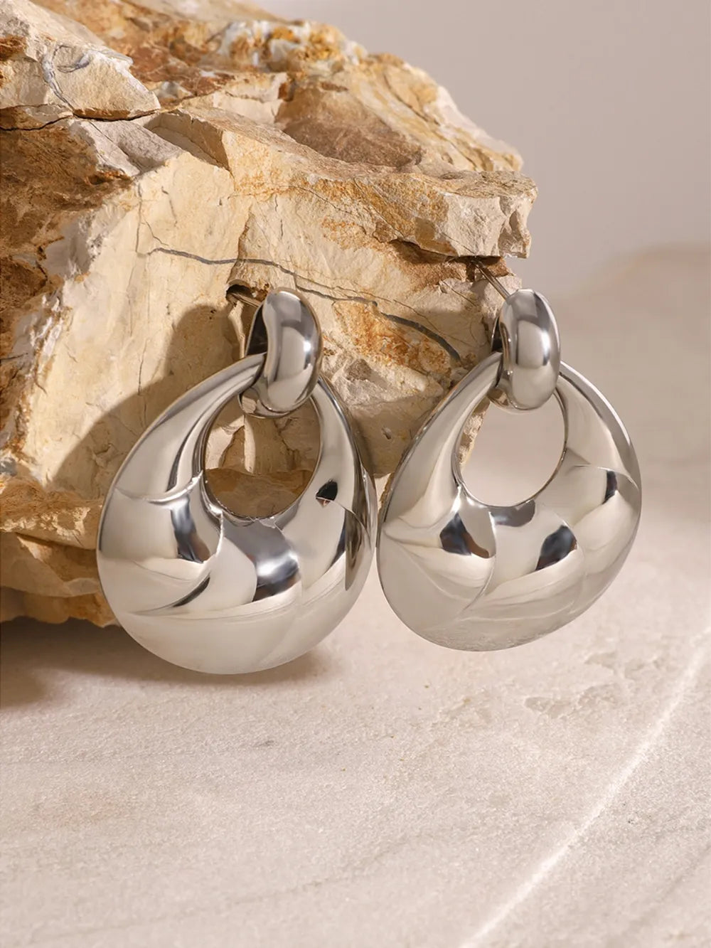 Silver hoop earrings on a stone surface