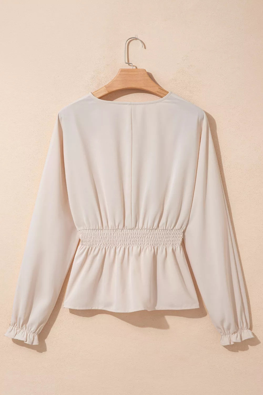 White blouse on a wooden hanger against a beige background