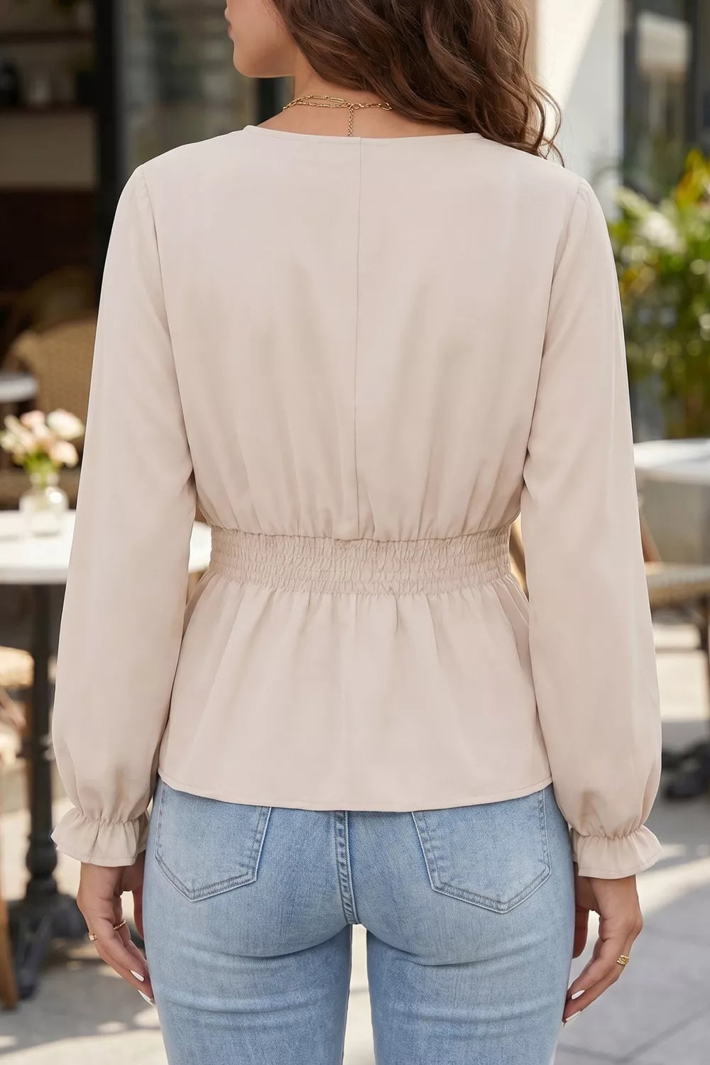 Woman wearing a beige blouse and blue jeans in an outdoor setting