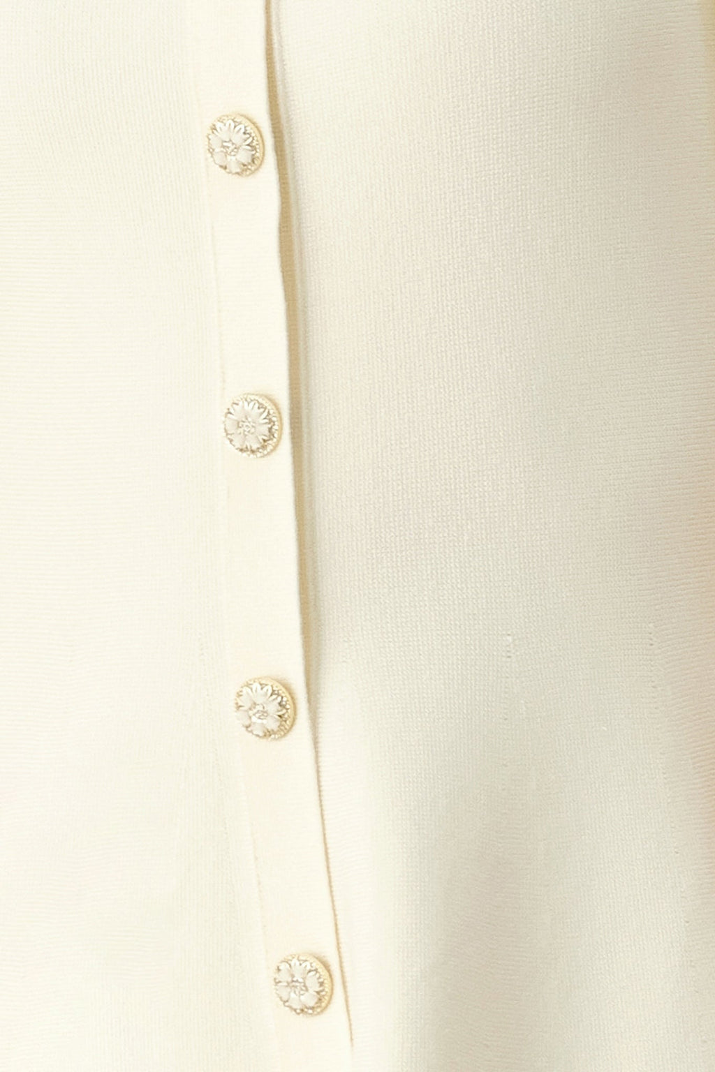 Close-up of a cream-colored garment with decorative buttons on a white background