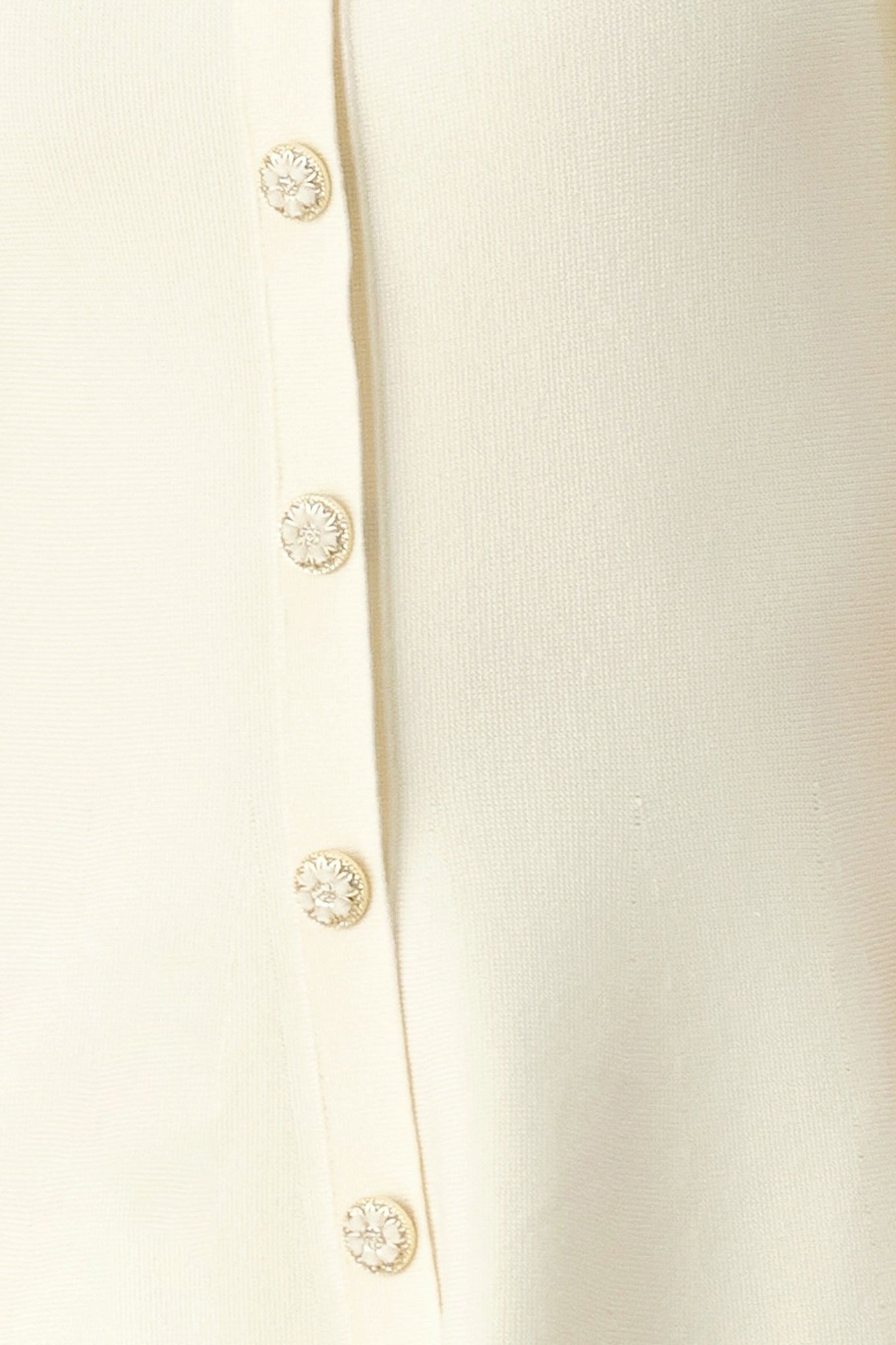 Close-up of a cream-colored garment with decorative buttons on a white background