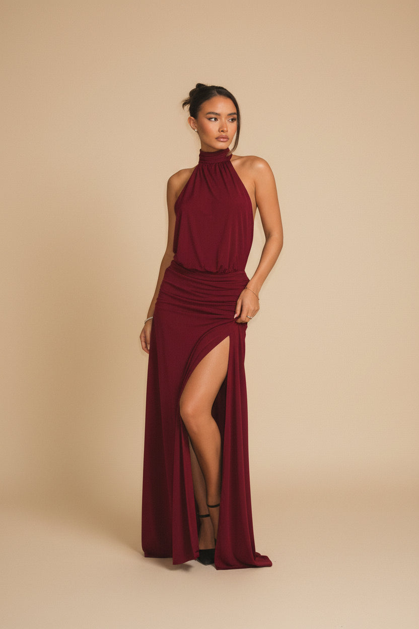 Woman wearing a burgundy halter neck dress with a slit, standing against a neutral background.