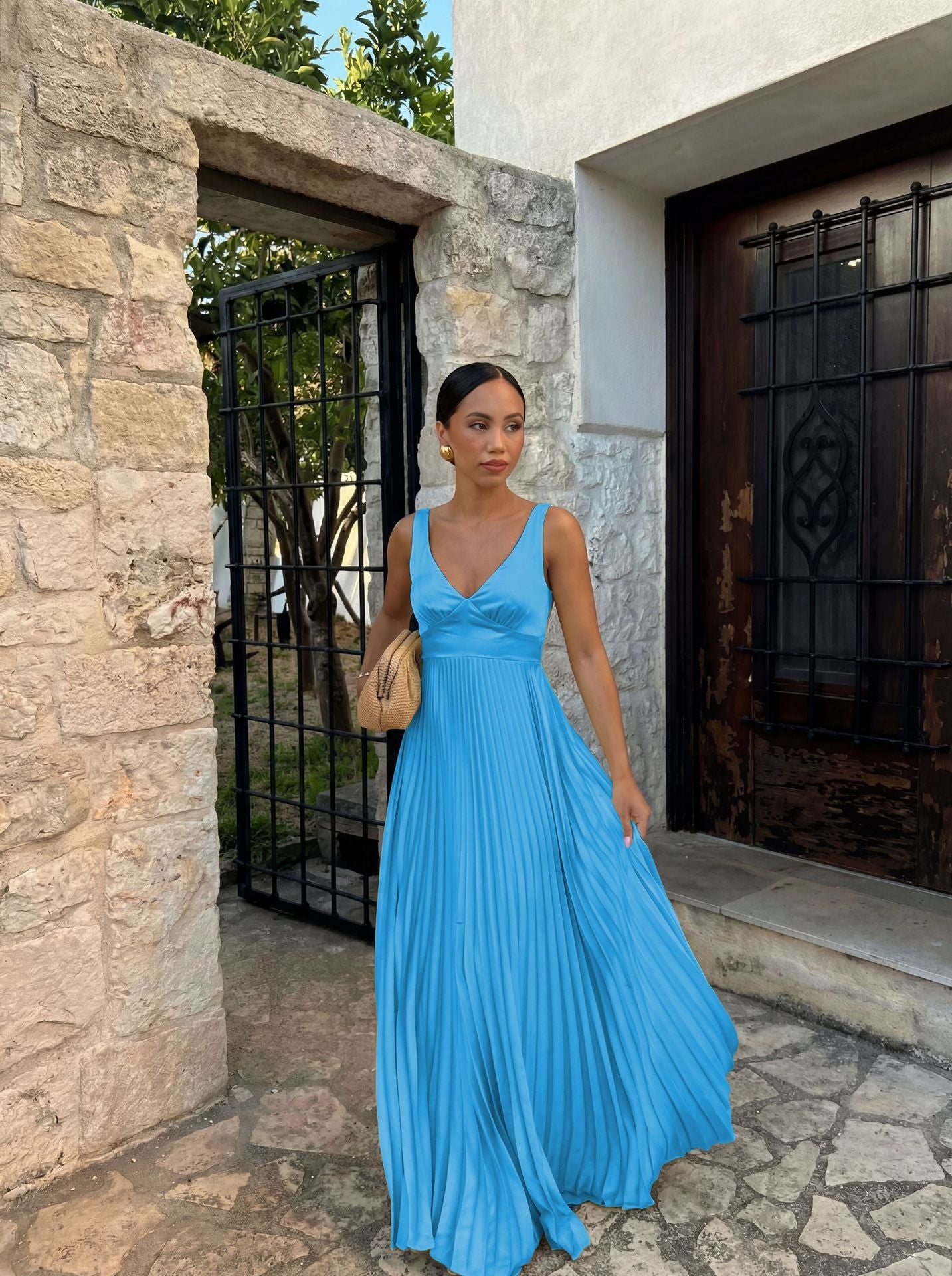 Woman in a blue dress standing in front of a stone wall and metal gate.
