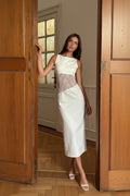 Woman in a white dress with lace details standing in a doorway.
