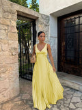Woman in a yellow dress standing in front of a stone wall and metal gate.