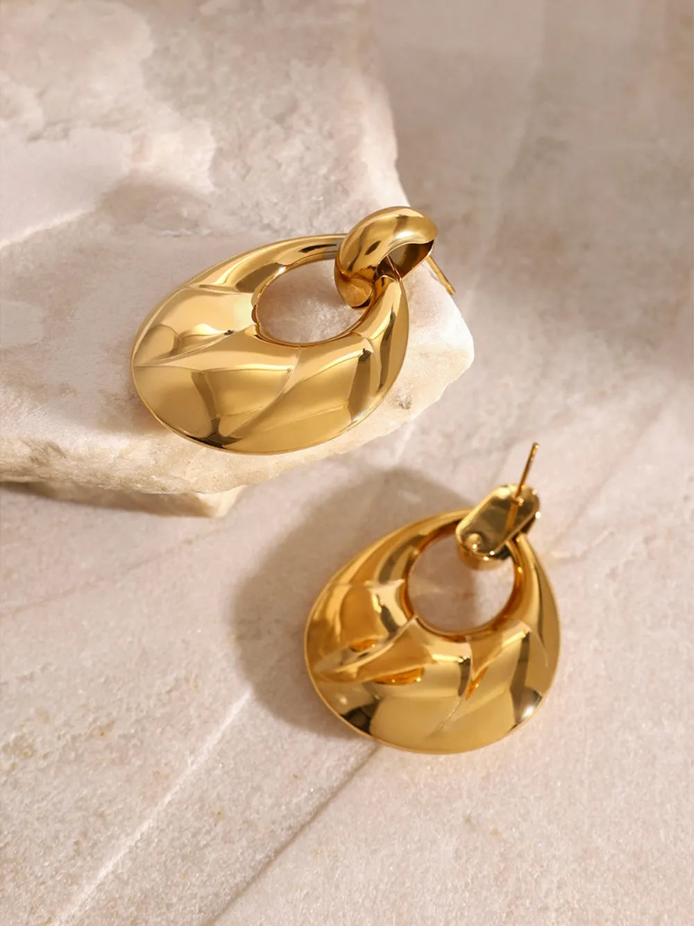 Gold hoop earrings on a light stone surface