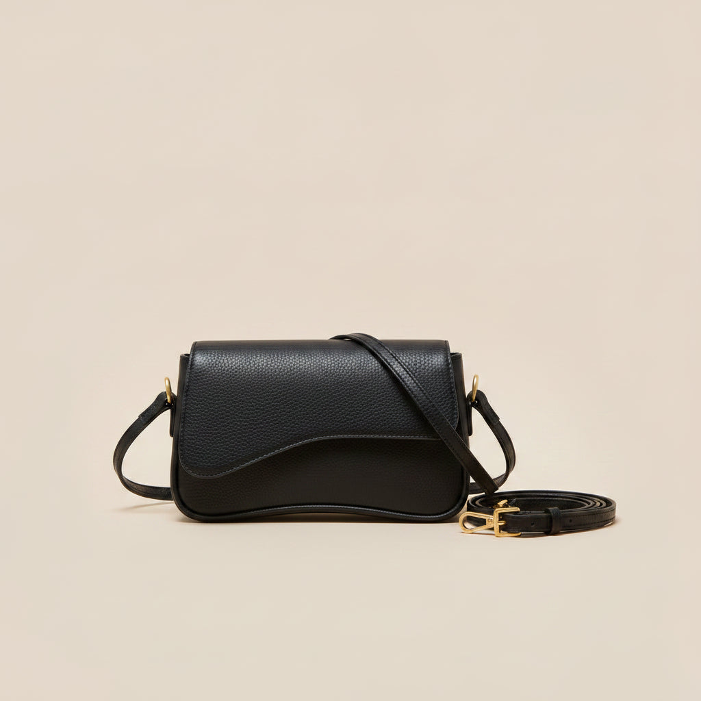 A black pebbled leather crossbody handbag with a curved front flap and a thin shoulder strap, shown against a solid beige background.