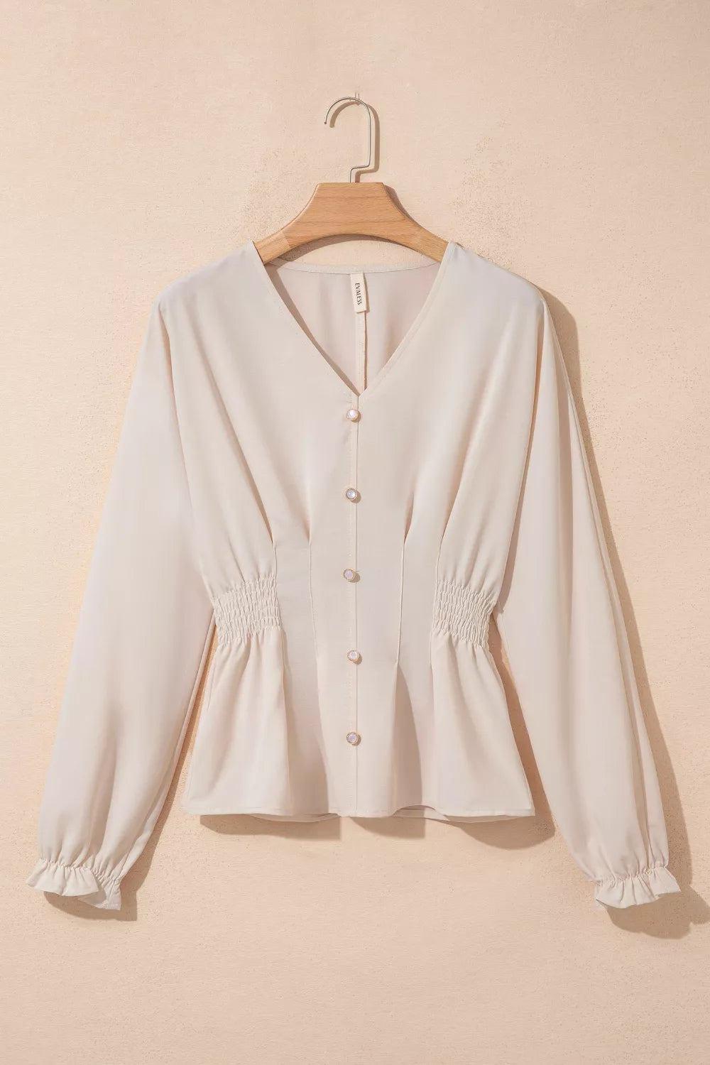 White blouse on a wooden hanger against a beige background