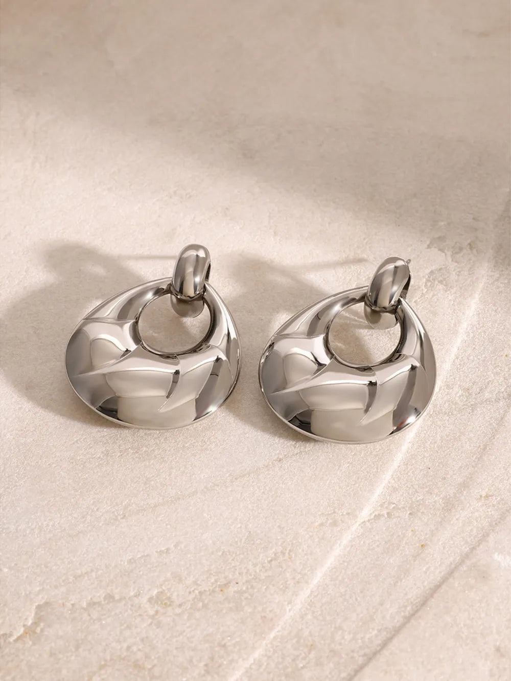 Pair of silver earrings on a light stone surface