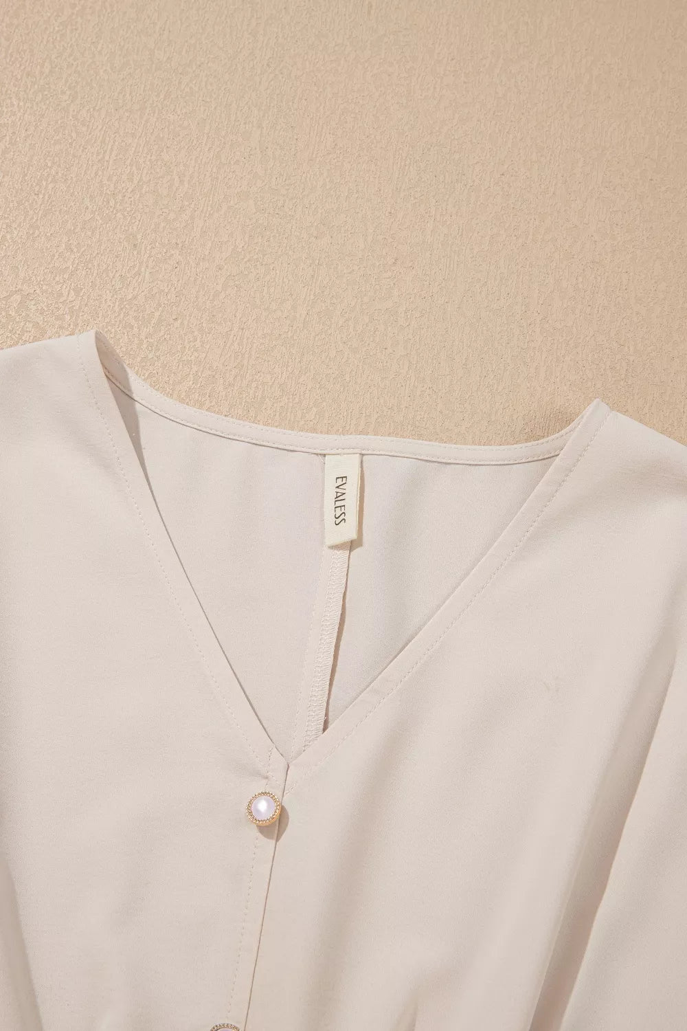 Close-up of a beige cardigan with a brand label on a beige background