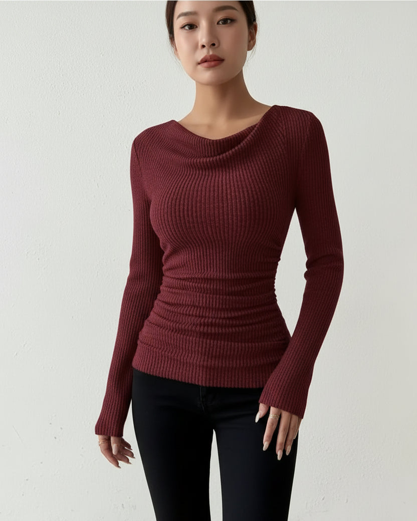 Person wearing a maroon ribbed sweater against a white wall.